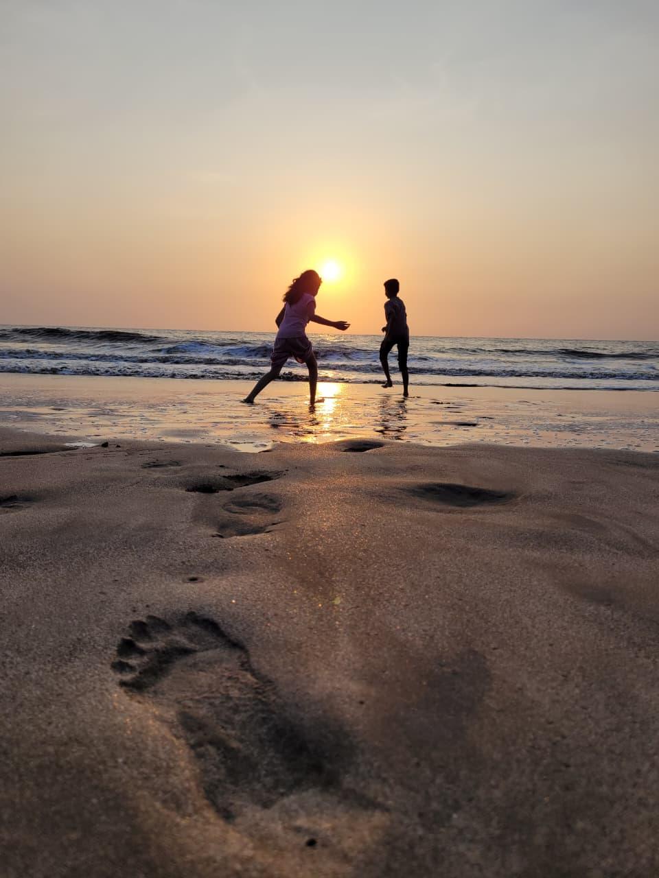 Two kids playing in the shallows at sunset, a footprint in the sand up close