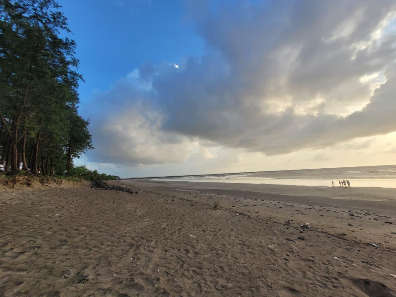 Storm clouds rolling over a wide, empty beach lined with trees
