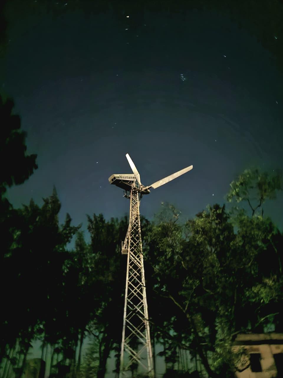 A wind turbine lit up against a starry night sky above the trees